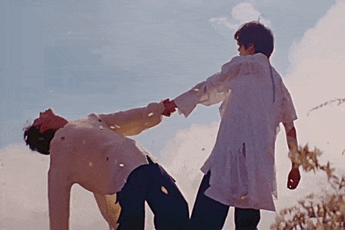 two men are holding hands in a field and one is laying on his back .