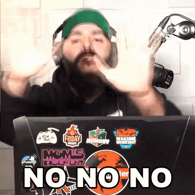 a man wearing headphones and a green hat stands in front of a laptop that says no no no