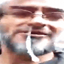 a man with glasses and a beard is smoking a cigarette in a close up of his face .