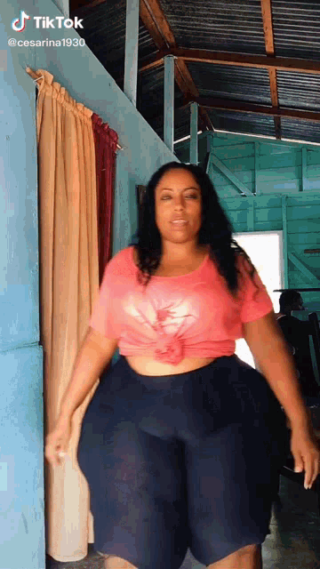 a woman in a pink shirt and black shorts is standing in a room with a blue wall .