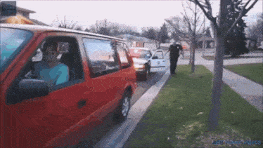 a red van is parked on the side of the road next to a tree