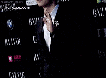 a man in a suit is standing on a red carpet in front of a wall that says bazaar .