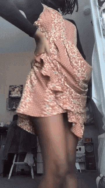 a woman in a pink floral dress is standing in a room with a speaker in the background