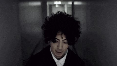 a young man with curly hair is standing in a dark hallway .