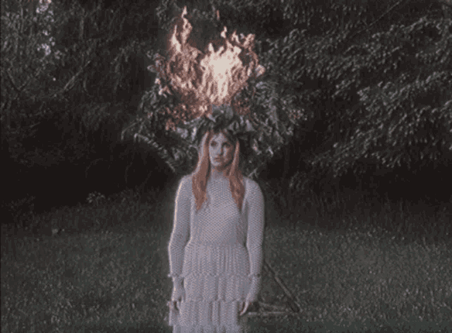 a woman in a white dress standing in front of a fire