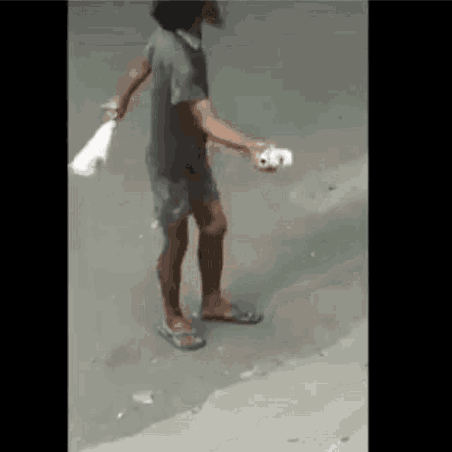 a man in flip flops is standing on the sidewalk holding a tissue .