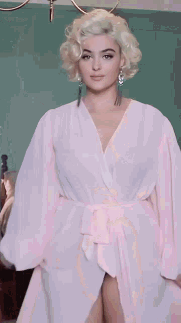 a woman in a white robe is standing in front of a bed .
