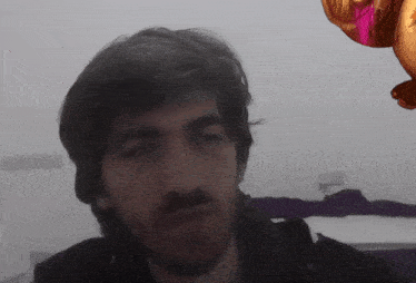a man with a beard is looking at the camera with a pink balloon in the background