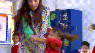 a woman in a colorful dress is standing next to a girl in a red shirt in a classroom .