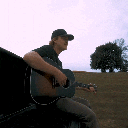 a man playing a guitar in a field with a tree in the background