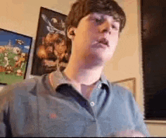 a young man in a blue shirt is standing in front of a wall with a picture on it .