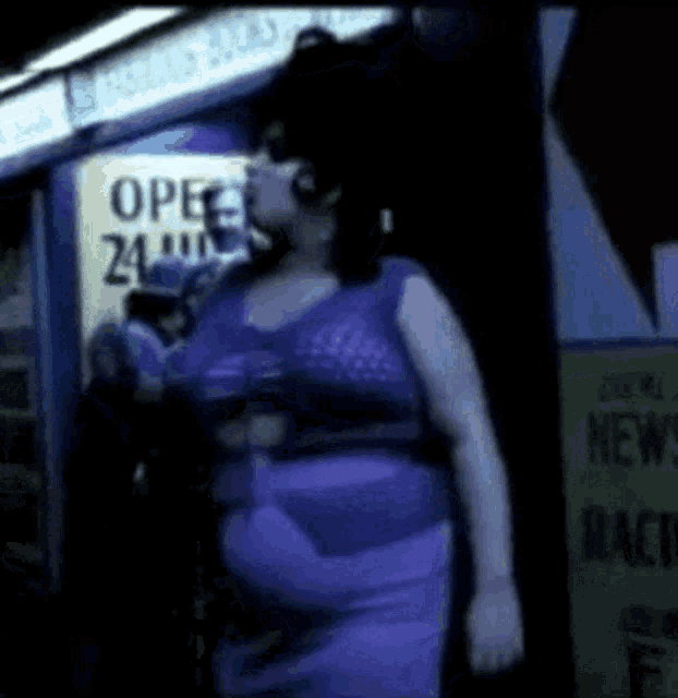 a woman in a purple dress is standing in front of a store that is open 24 hours