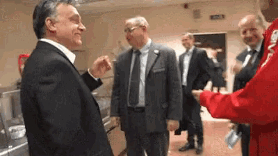 a man in a suit is talking to another man in a red shirt that says ' sns ' on it