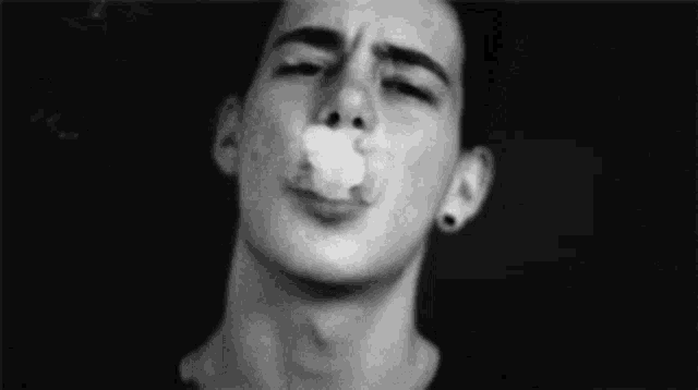 a man is smoking a cigarette with smoke coming out of his mouth .