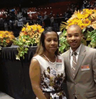 a man in a suit and tie poses with a woman in a floral dress in front of flowers