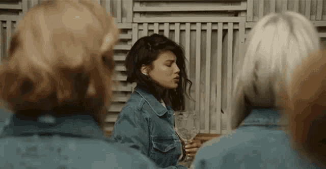 a woman in a denim jacket is holding a glass of wine in front of a group of women in denim jackets .