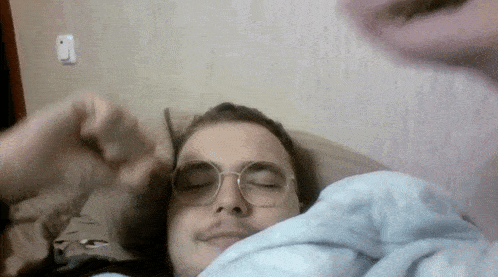a man wearing glasses is laying in a bed with his eyes closed