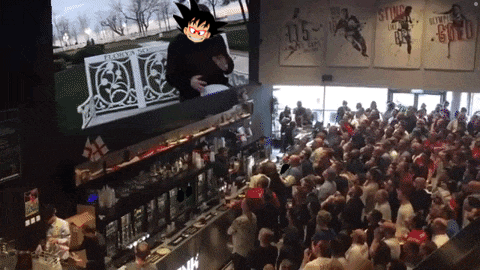 a crowd of people are gathered in front of a large screen with a cartoon character on it that says ' goku '