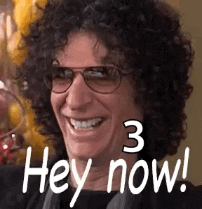 a man with curly hair and glasses is smiling and saying hey now .