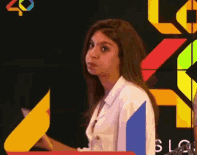 a woman in a white shirt is standing in front of a colorful background with the word slo on it