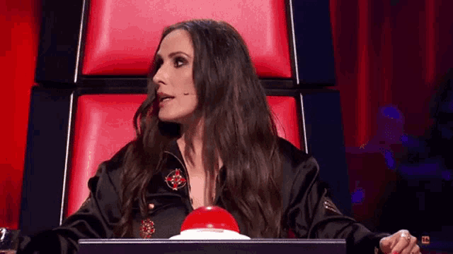 a woman in a black jacket is sitting in a red chair holding a red button