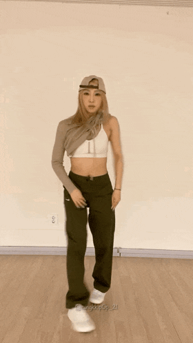 a woman wearing a hat and a crop top is dancing on a wood floor .