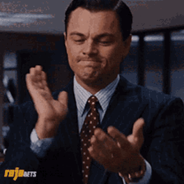 a man in a suit and tie is clapping his hands with rojabets written on the bottom