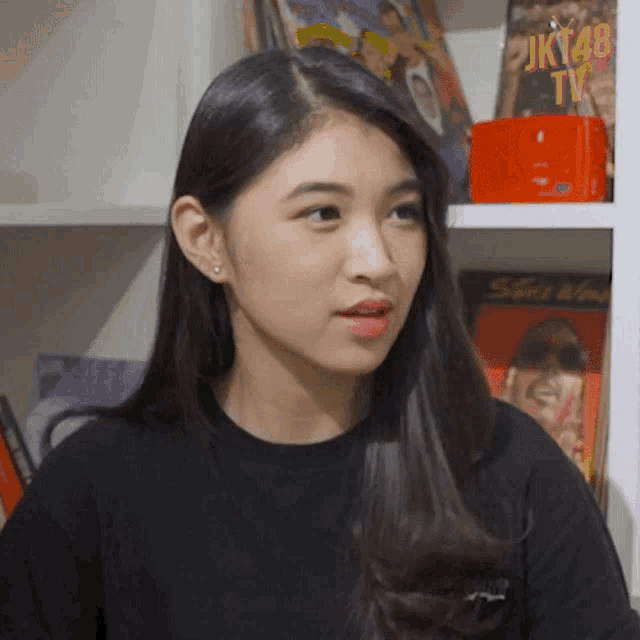 a woman in a black shirt stands in front of a shelf with magazines on it including jkt48 tv