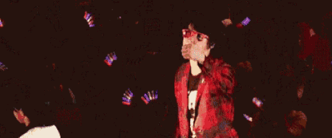 a man in a red jacket is dancing in front of a crowd with confetti falling around him .