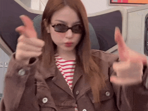 a woman wearing sunglasses and a brown jacket is giving a thumbs up