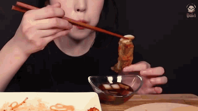 a person is eating food with chopsticks and dipping it into sauce .