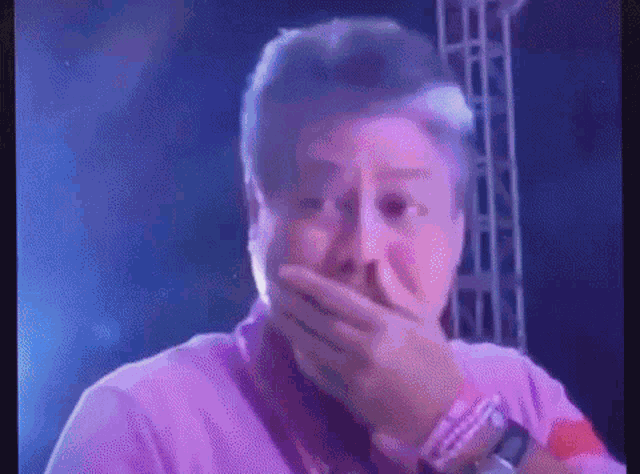 a man in a pink shirt is covering his mouth with his hand while standing on a stage .