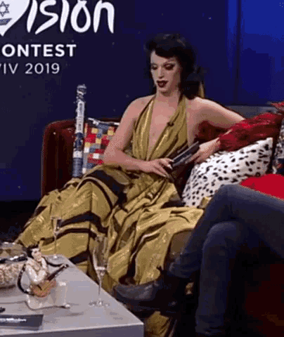 a woman in a gold dress is sitting in front of a sign that says vision contest iv 2019