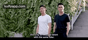 two men are standing next to each other in front of a hedge and a staircase .