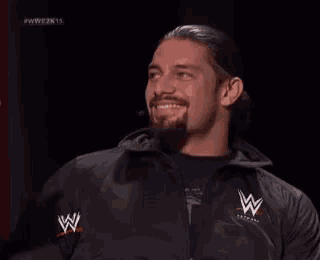 a man with a beard is wearing a black jacket with a w logo on it .