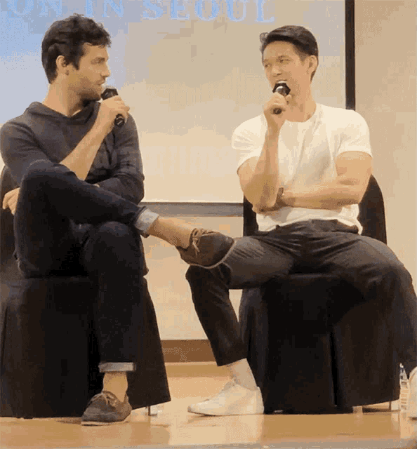 two men sit in front of a screen that says seoul on it