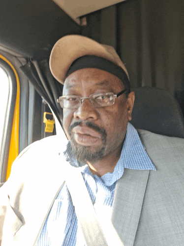 a man wearing glasses and a hat is sitting in the driver 's seat of a car