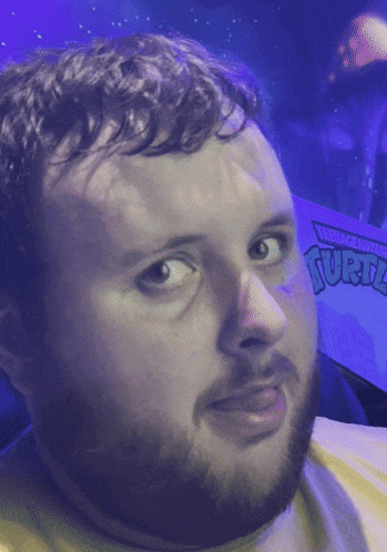 a man with a beard and a teenage mutant ninja turtles sign in the background