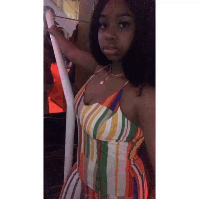a woman in a colorful striped dress is leaning against a pole .
