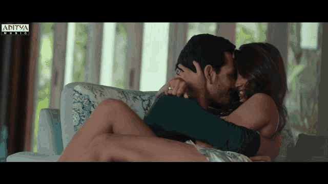 a man and woman kissing on a couch with aditya music written on the bottom of the screen