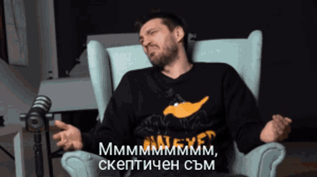 a man sitting in a chair wearing a black sweater that says mmmmm