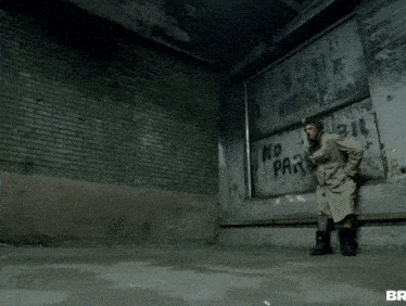 a man in a trench coat stands in front of a wall that says no parking