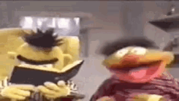 two sesame street characters , bert and elmo , are sitting next to each other and laughing .