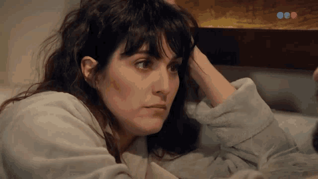 a woman in a bathrobe is laying on a bed with a red and blue circle in the upper right corner