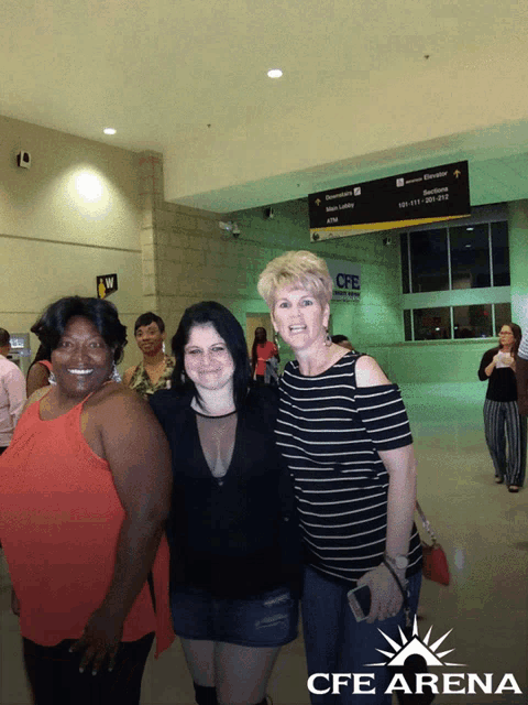 three women are posing for a photo in front of a cfe arena sign