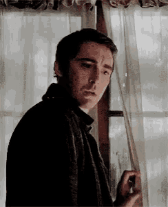 a man is standing in front of a window holding a cigarette .