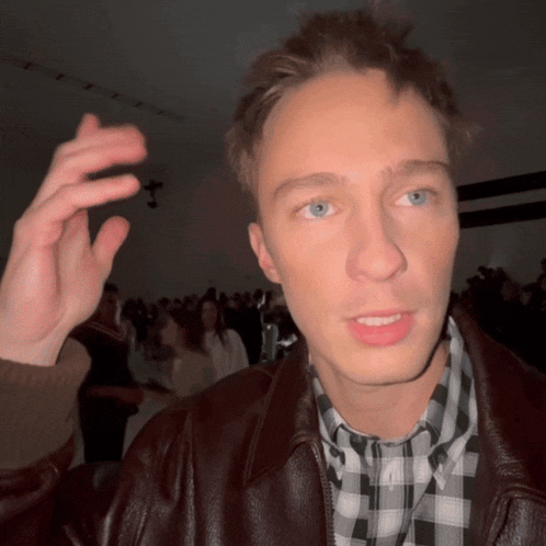 a man wearing a plaid shirt and a leather jacket looks at the camera