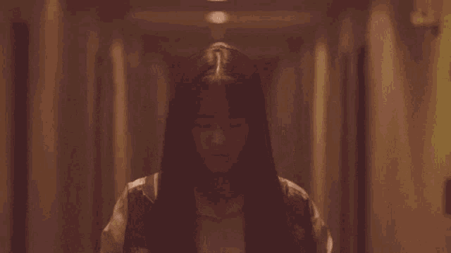 a woman with long hair is walking down a hallway .