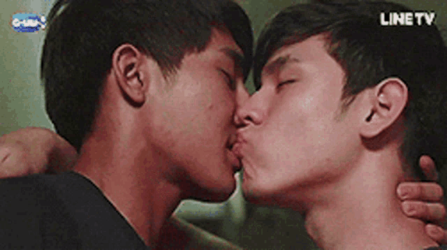 two young men are kissing in front of a line tv sign .