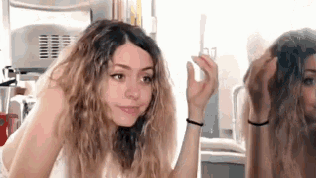 a woman is looking at her hair in front of a mirror in a bathroom .